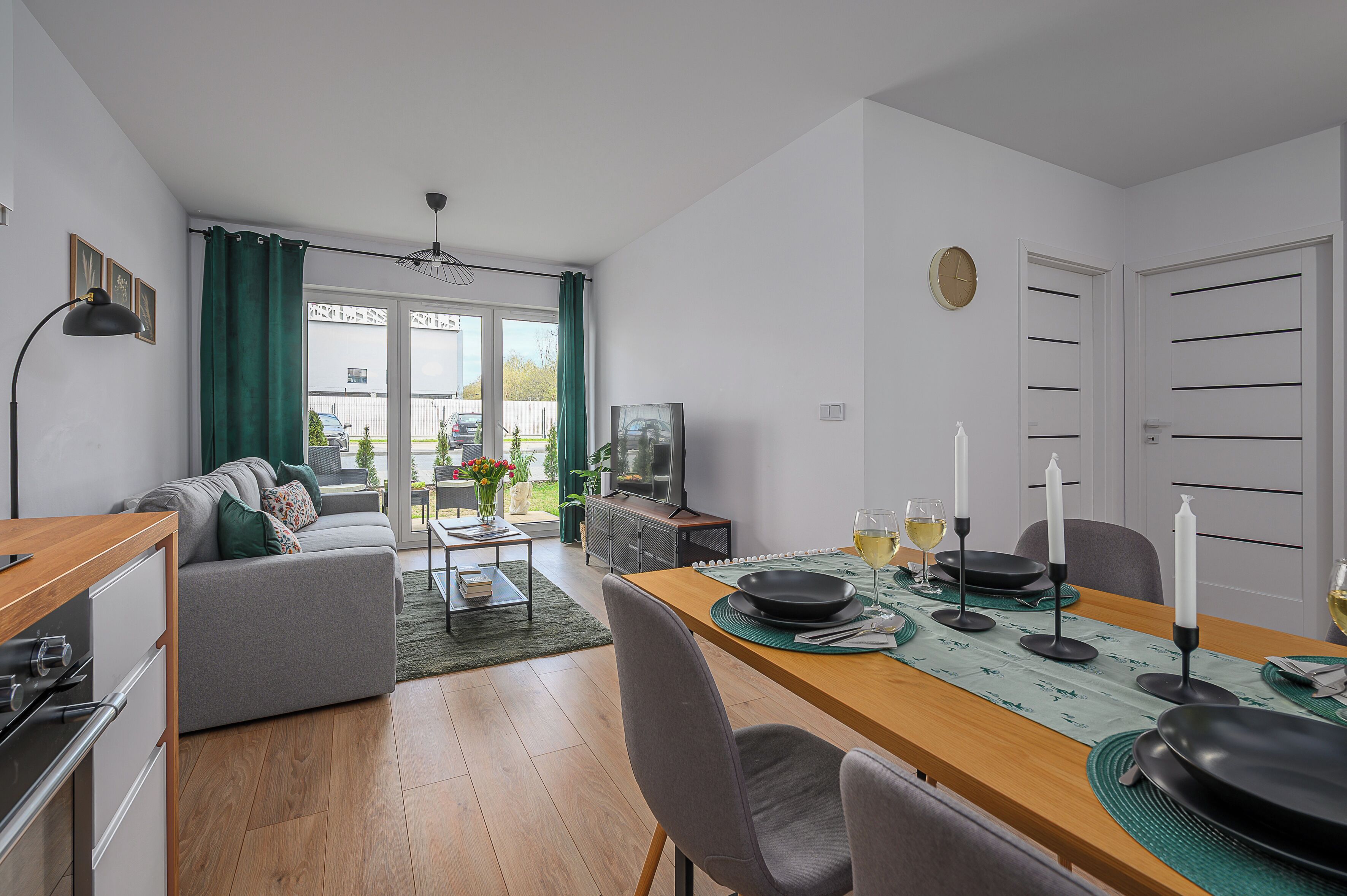 A modern living room with a dining area, a sofa, a TV, and a view of the outside.
