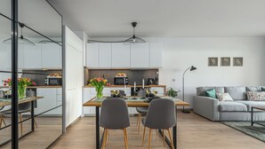 Une cuisine moderne avec des meubles blancs, une table à manger avec des chaises et un canapé gris dans l’espace salon.