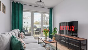Un salon moderne avec un canapé gris, une table basse, un téléviseur et une porte-fenêtre coulissante donnant sur un espace extérieur.