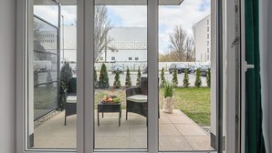 On aperçoit, à travers une porte-fenêtre coulissante, un espace extérieur aménagé en terrasse, avec une table, des chaises et un petit sapin de Noël.