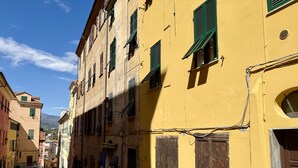 A narrow street with yellow buildings, parked cars, and a clear sky. - Casa di Ada (Imperia)