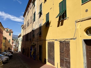 Un carrer estret amb edificis grocs, cotxes aparcats i un cel clar.