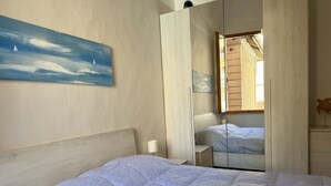 A bedroom with a bed, a nightstand, a lamp, a painting, and a window with wooden shutters. - Casa di Ada (Imperia)