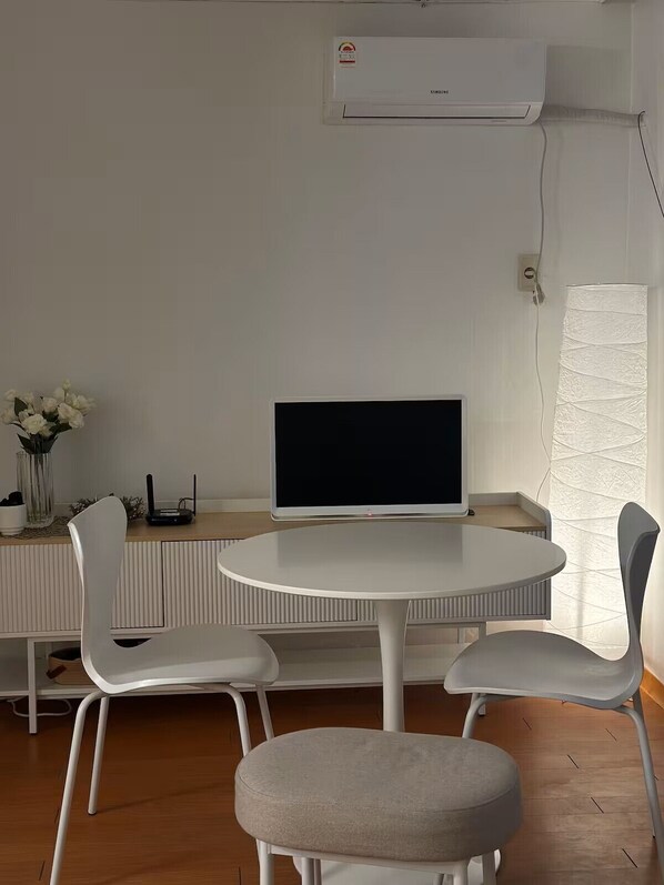A modern room with a round table, two chairs, a flat-screen TV, an air conditioning unit, and a decorative vase with flowers. - JS building 403 (Seoul)