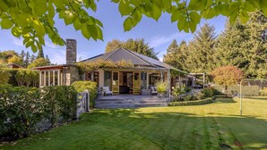 Ein Haus mit überdachter Veranda, einem Steinkamin und einem gepflegten Rasen.