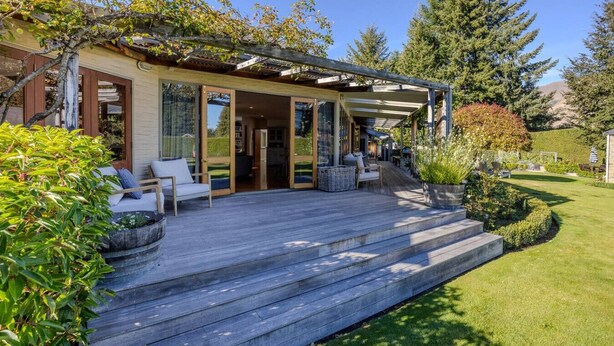 Ein modernes Haus mit Holzterrasse, Sitzgelegenheiten im Freien und einem gepflegten Garten.
