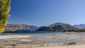 Blick auf einen See mit Bergen im Hintergrund, ein Sandstrand und eine Bank.