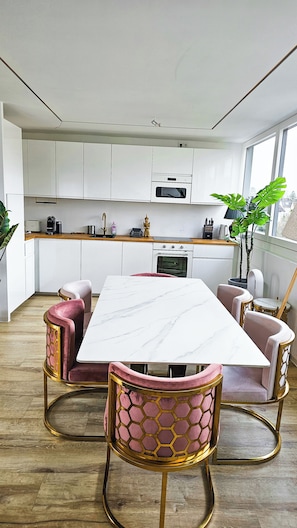 Una cocina moderna con armarios blancos, una mesa de comedor de mármol y sillas tapizadas en rosa.
