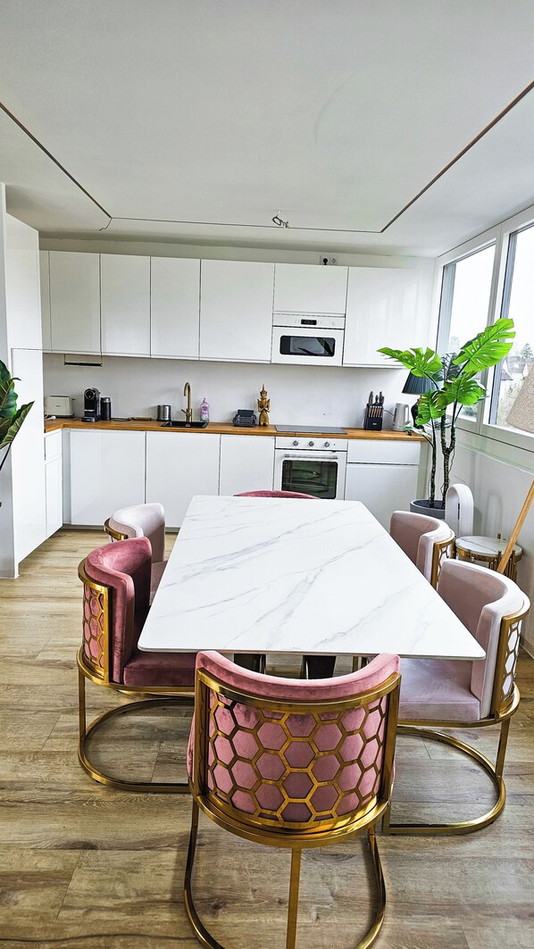 Una cucina moderna con mobili bianchi, un tavolo da pranzo in marmo e sedie imbottite rosa.