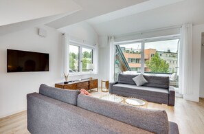 Een moderne woonkamer met een grijze bank, een salontafel en een aan de muur bevestigde televisie.