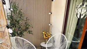 A patio with two white wire-framed chairs, a patterned rug, a wooden slatted wall, and a glass door with a decorative metal piece. - Cozy apartment near Lake Constance - ideal for couples (Friedrichshafen)