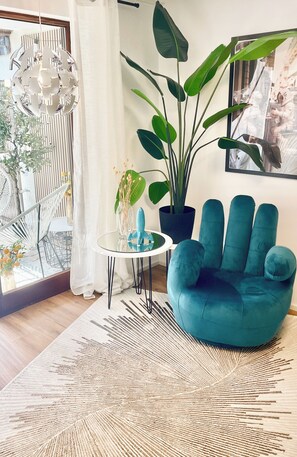 A modern living room with a blue armchair, a large potted plant, a glass table with a sculpture, and a hanging light fixture. - Cozy apartment near Lake Constance—perfect for couples   (Friedrichshafen)