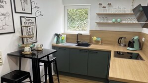 A modern kitchen with a wooden countertop, black bar stools, and a window with a view of greenery. - Cozy apartment near Lake Constance - ideal for couples (Friedrichshafen)