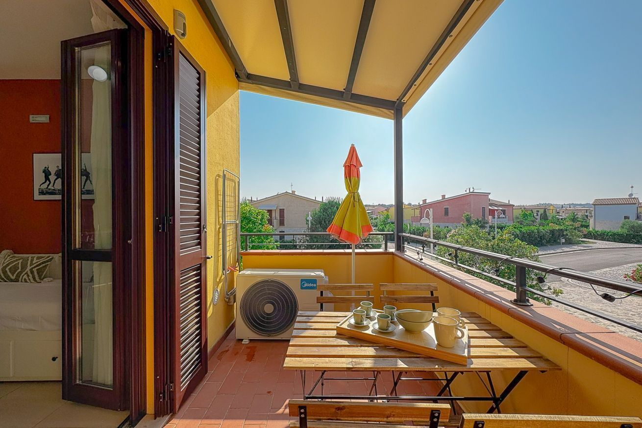 Varanda com mesa posta para refeições, um ventilador e vista para edifícios.