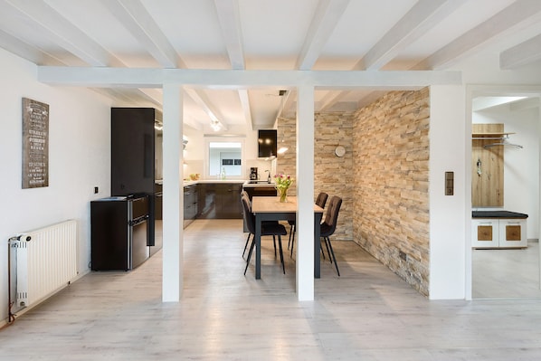 An open-plan kitchen with a stone wall, a dining area with chairs, and a refrigerator.