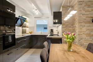 A modern kitchen with dark cabinetry, a wooden dining table, and a vase of flowers.