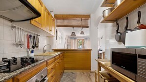 A kitchen with wooden cabinets, a built-in stove, hanging utensils, and a large TV. - Casita Abrilcon with Garden (Cap Roig)