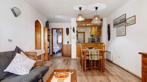 A living room with a sofa, coffee table, dining table with chairs, kitchen area, and a hallway leading to a bedroom. - Casita Abrilcon with Garden (Cap Roig)