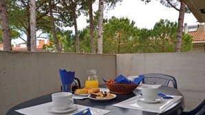 Une table mise pour le petit-déjeuner, avec un panier, des assiettes, des tasses et un pichet de jus d’orange.