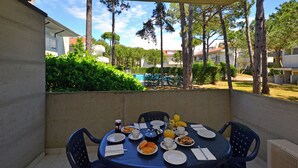 Eine überdachte Terrasse mit einem Tisch, der für ein Frühstück gedeckt ist, einschließlich Tellern, Tassen und einem Wasserkocher.