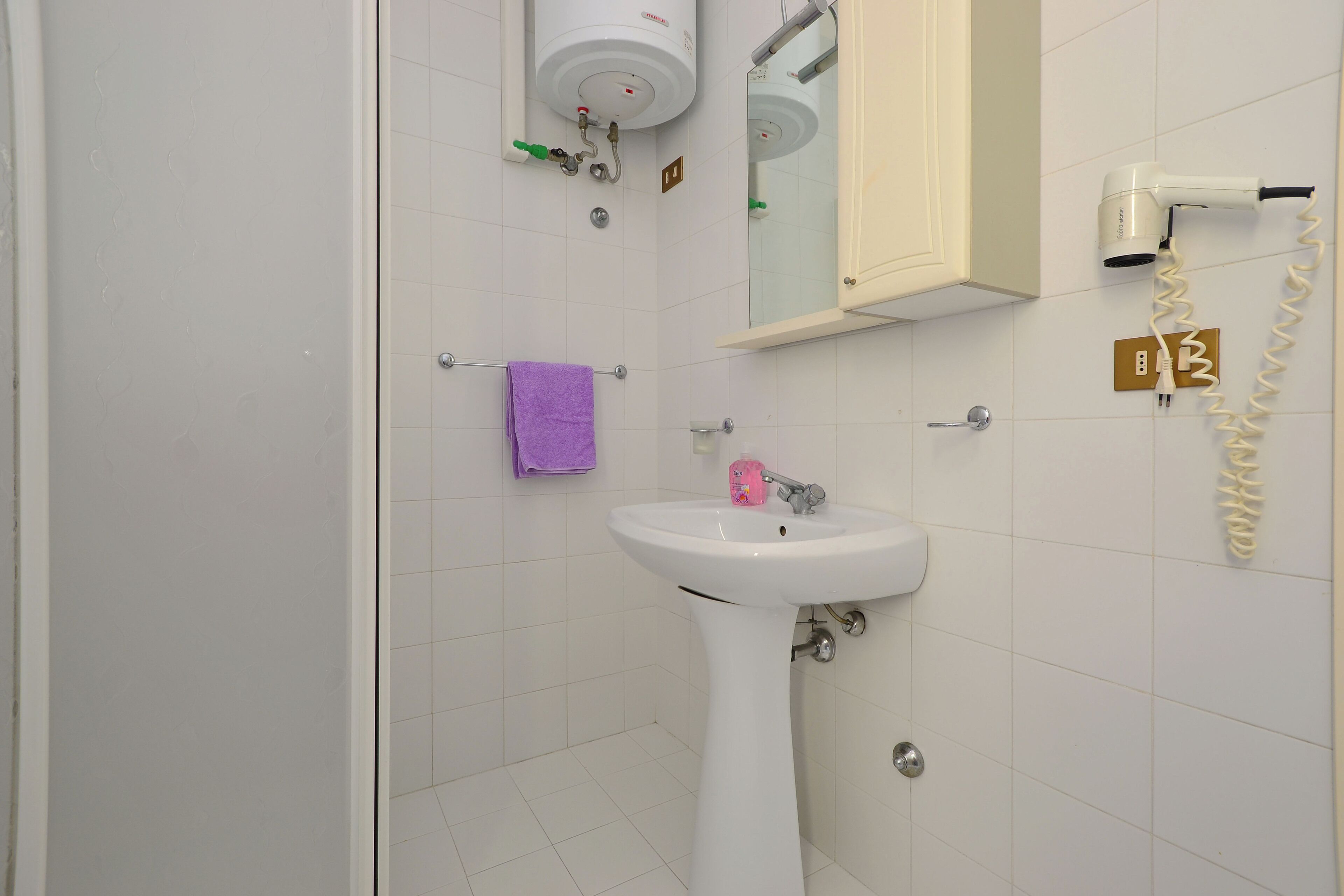 A bathroom with a white sink, a purple towel, a hairdryer, and a mirror.