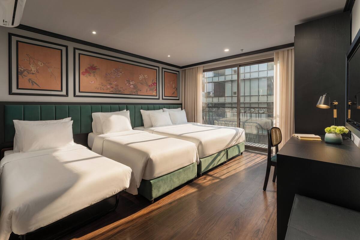A hotel room with two beds, a desk, a chair, and large windows with curtains.