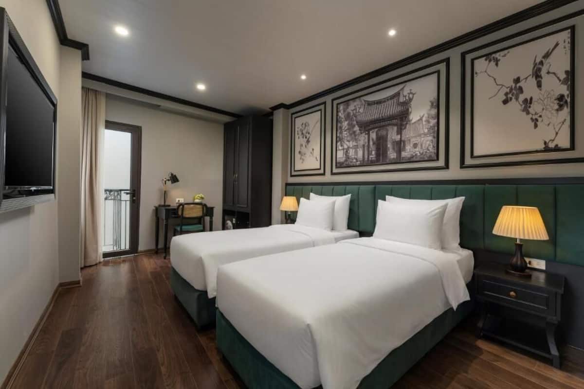 A hotel room with two beds, a television, a desk, and artwork on the walls.