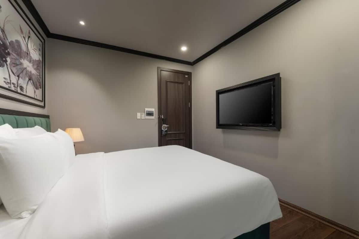 A hotel room with a bed, a television mounted on the wall, a door, and a wall-mounted light fixture.