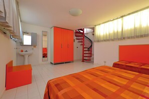 Un dormitorio con una cama, un armario rojo, un espejo, un lavabo y una escalera.