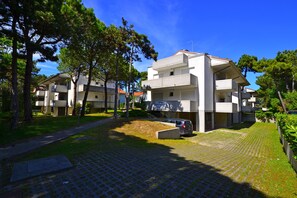 Un edificio residencial con un patio empedrado, un coche estacionado y árboles circundantes.