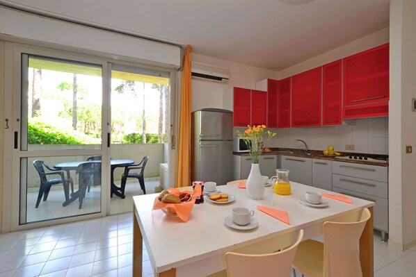Una cocina moderna con armarios rojos, un comedor con mesa y sillas, y vistas a un espacio exterior a través de una puerta de vidrio.