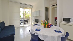 A dining area with a round table, chairs, a television, and a kitchen area with a microwave. - Cozy stay in Lignano (Lignano Sabbiadoro)