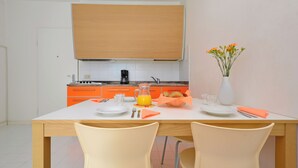 Ein Essbereich mit einem Tisch für zwei Personen, einer Kaffeemaschine, einer Blumenvase und orangefarbenen Schränken im Hintergrund.