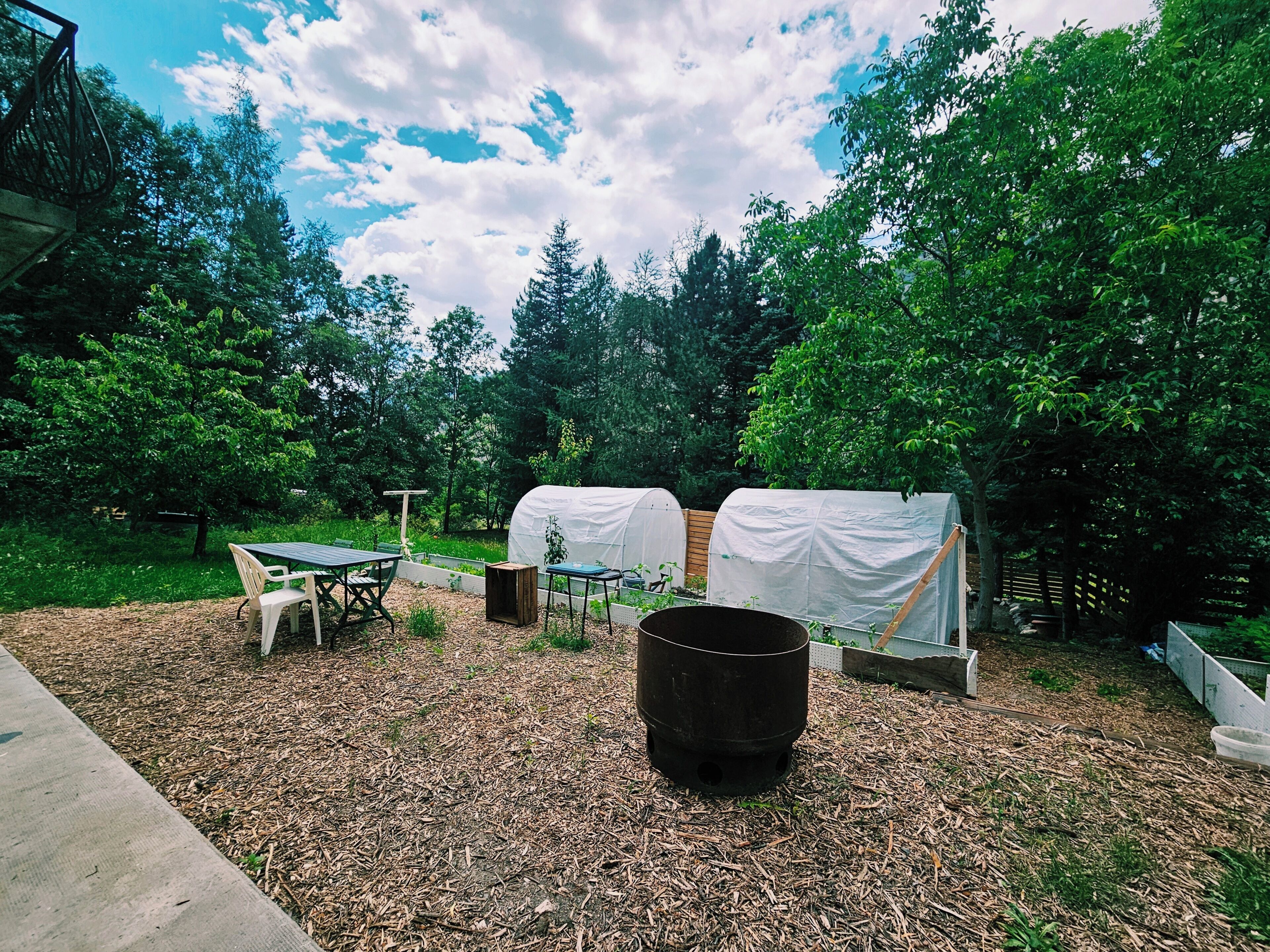 A covered outdoor area with a table and chairs, a trash bin, and a covered garden bed.