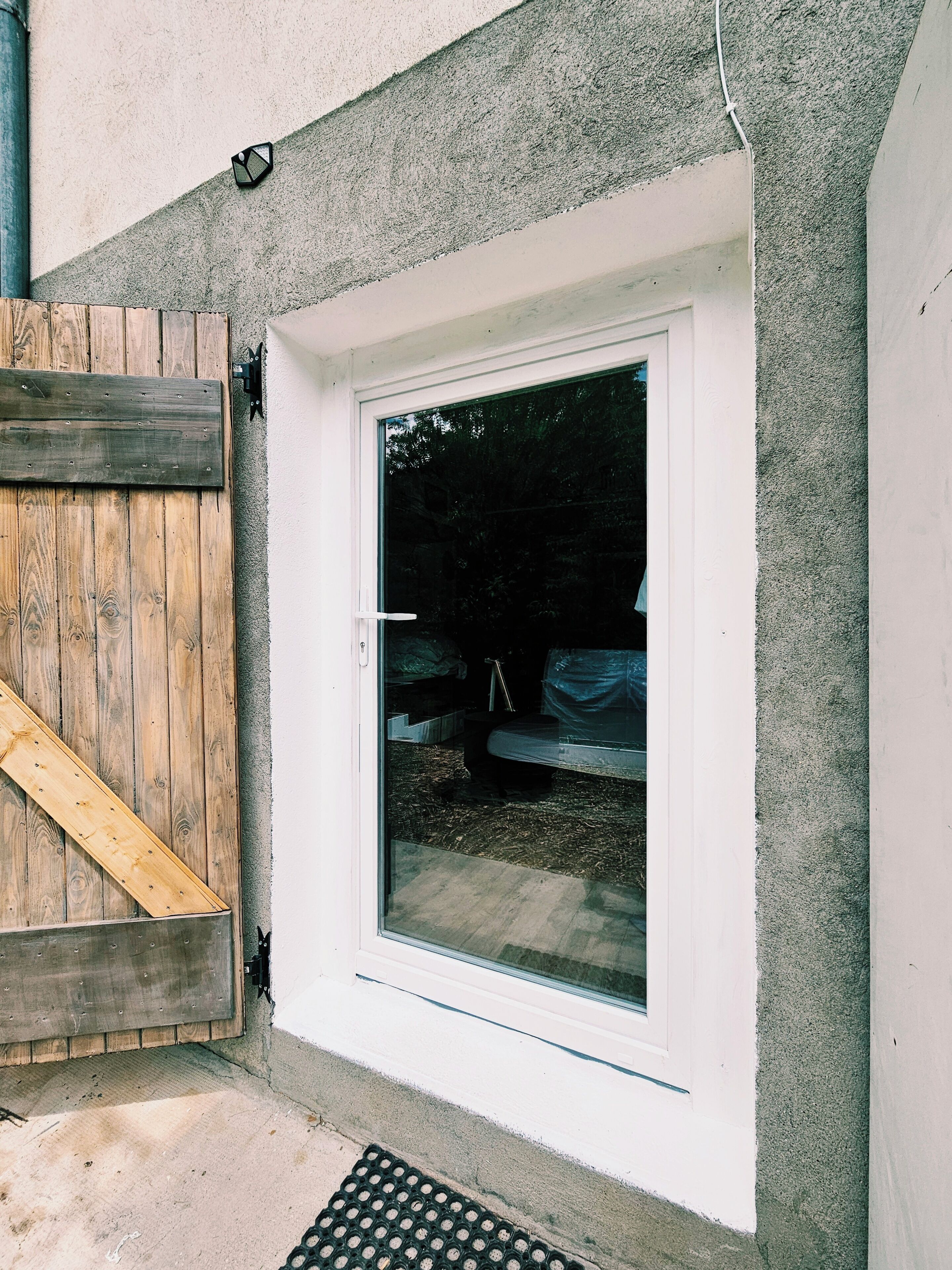 A window with a white frame and a clear glass pane, a wooden door with a metal handle, and a concrete wall.