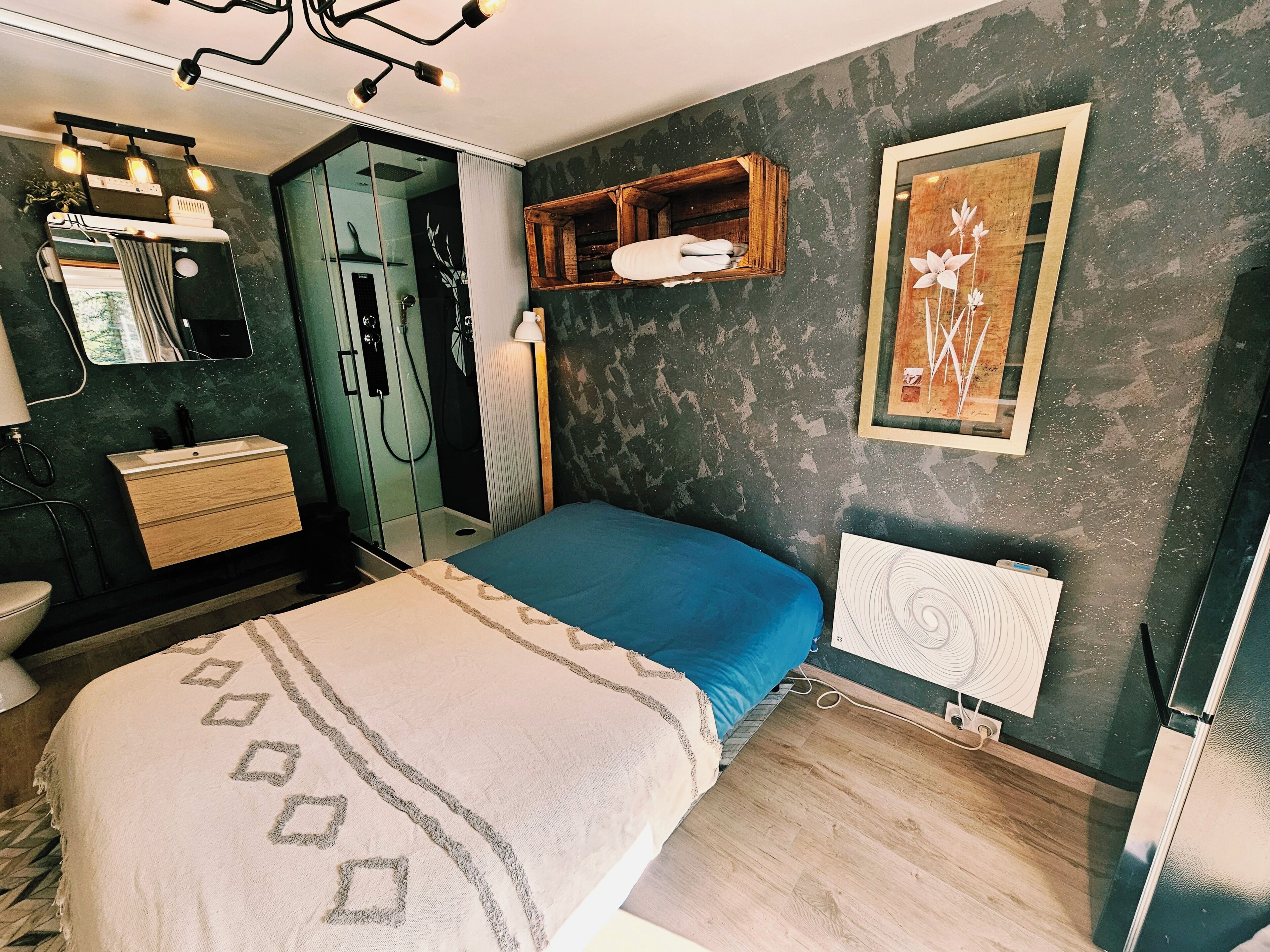 Une chambre à coucher avec un lit, une commode, un miroir, un radiateur et un tableau encadré accroché au mur.