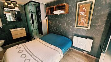 Une chambre à coucher avec un lit, une commode, un miroir, un radiateur et un tableau encadré accroché au mur.