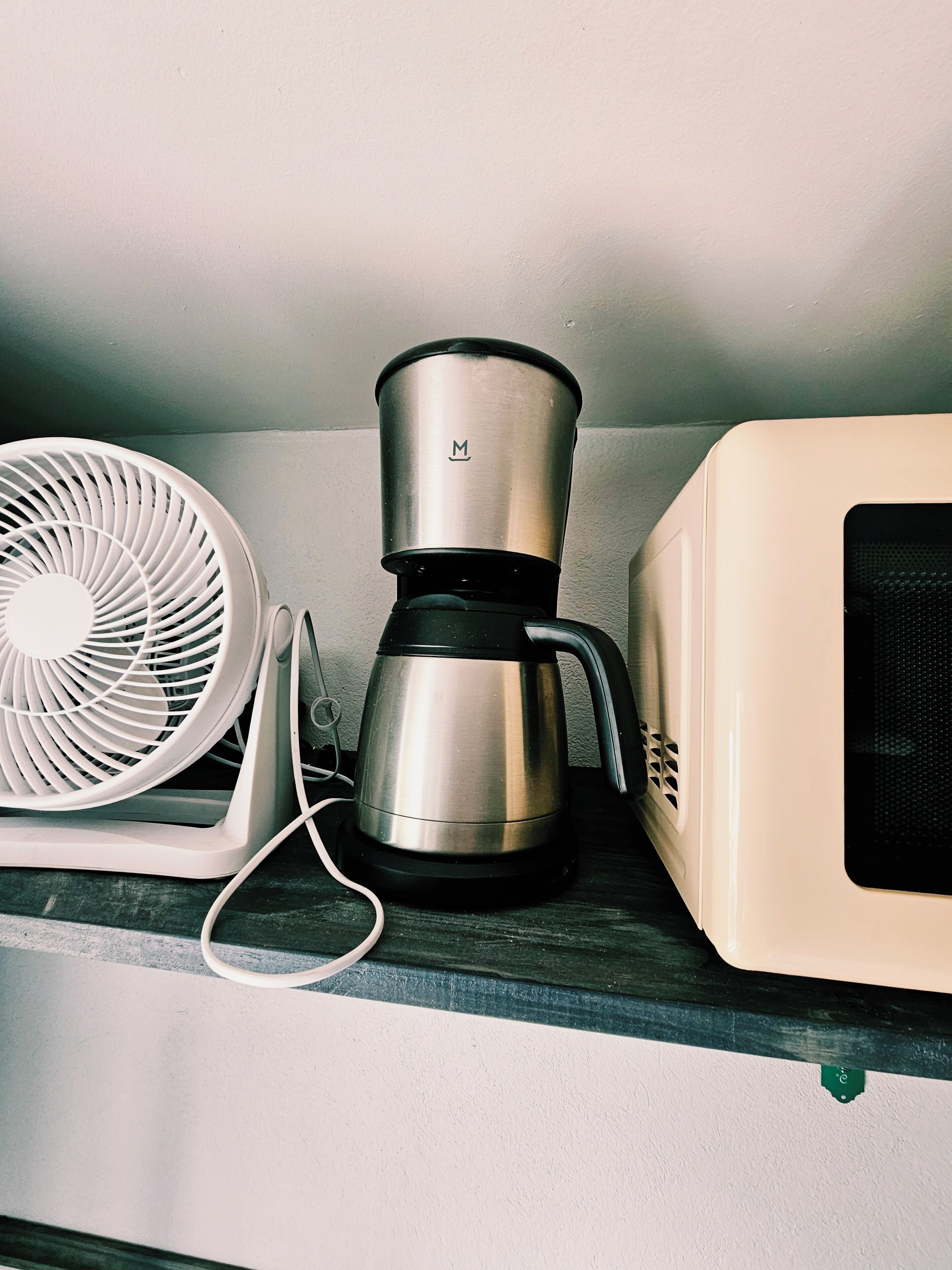 A kitchen with a white fan, a stainless steel coffee maker, and a white microwave on a countertop.