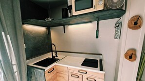 Uma cozinha compacta com pia, micro-ondas e ventilador.
