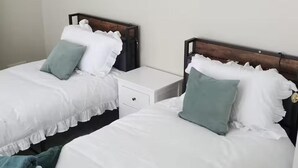 Deux lits jumeaux avec une literie blanche et des oreillers turquoise, chacun doté d’une tête de lit en bois et d’une table de chevet blanche.