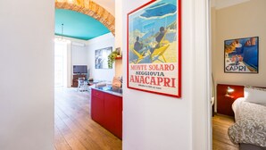A hotel room with a bed, a nightstand, a red cabinet, a kitchen area with a sink, and a dining area with chairs. - Quercia Design Home in the Center (Naples)