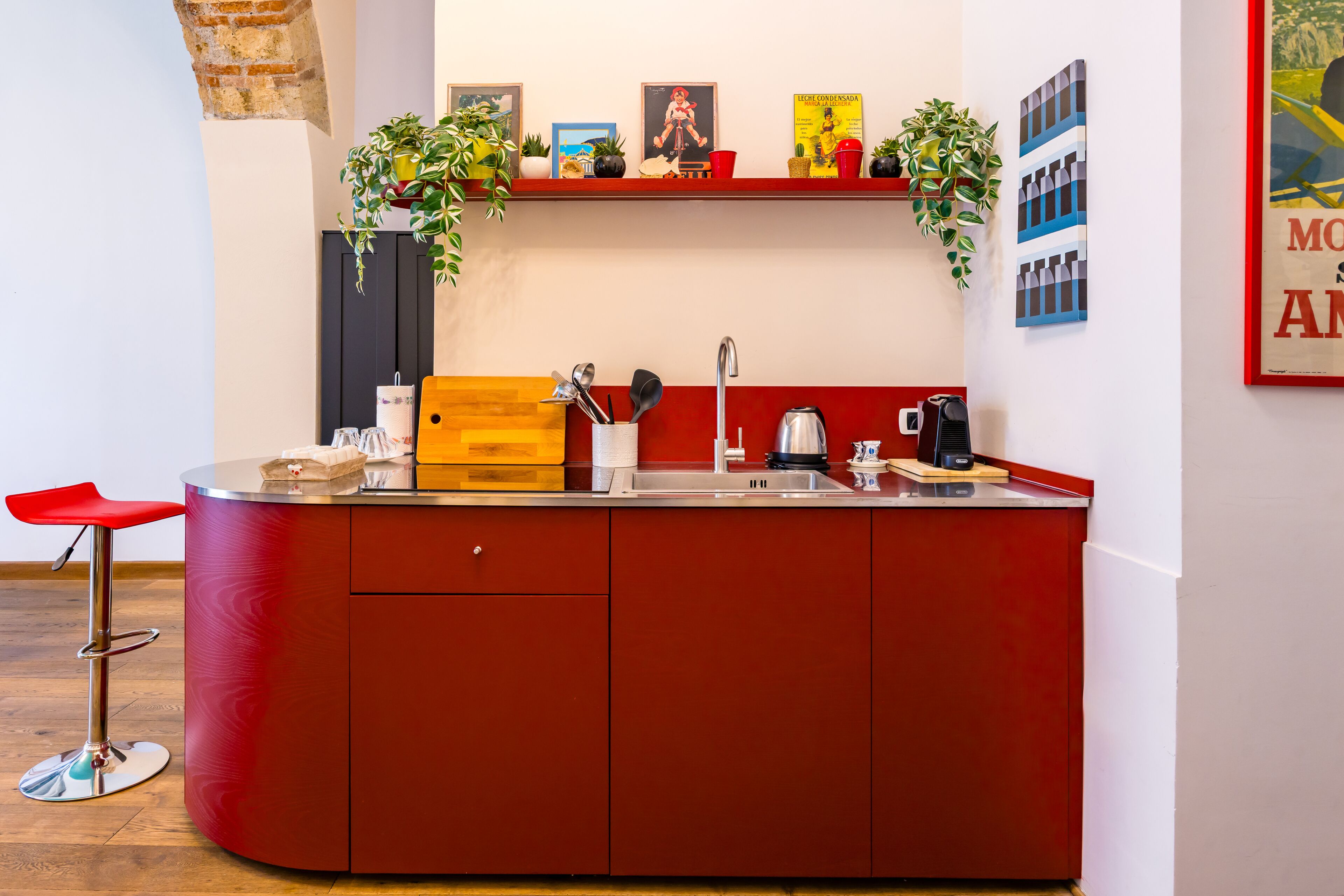 A compact kitchen with a red countertop, a sink, and a red bar stool.