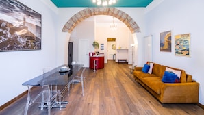 A modern living room with a glass dining table, a sofa, and a kitchen area visible through an archway. - Quercia Design Home in the Center (Naples)