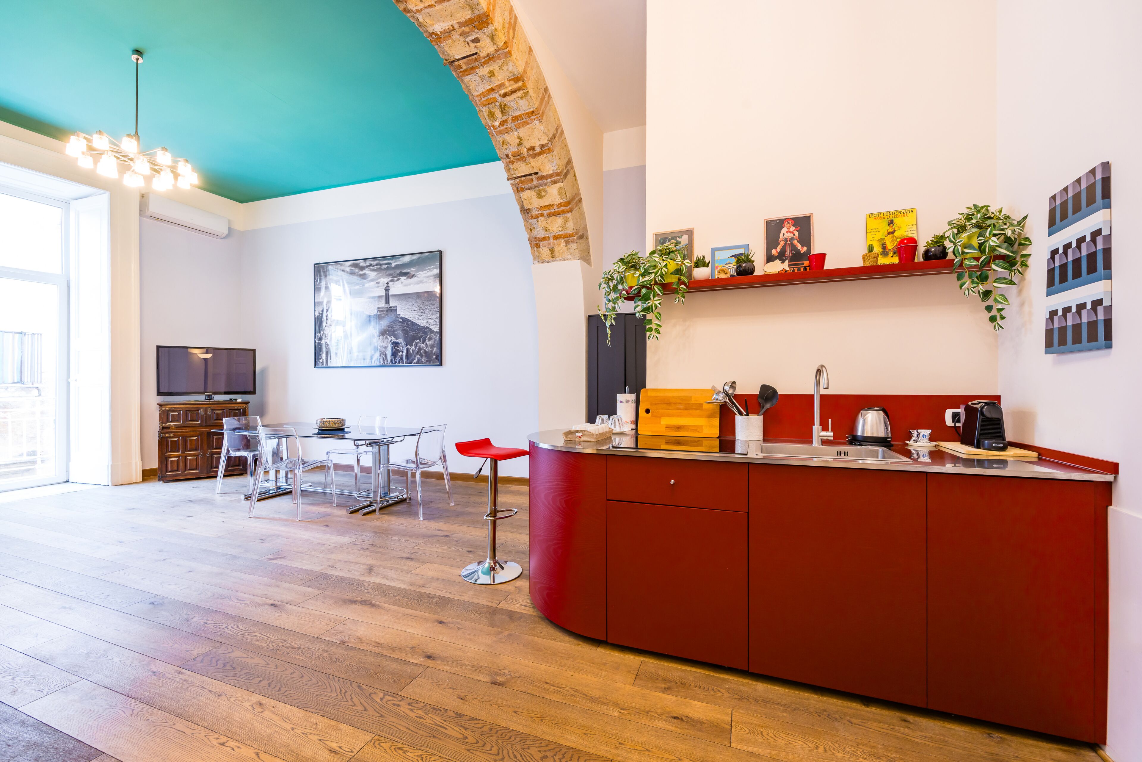 Una cocina moderna con una isla roja, una zona de comedor con sillas, un ventanal grande y una lámpara colgante.