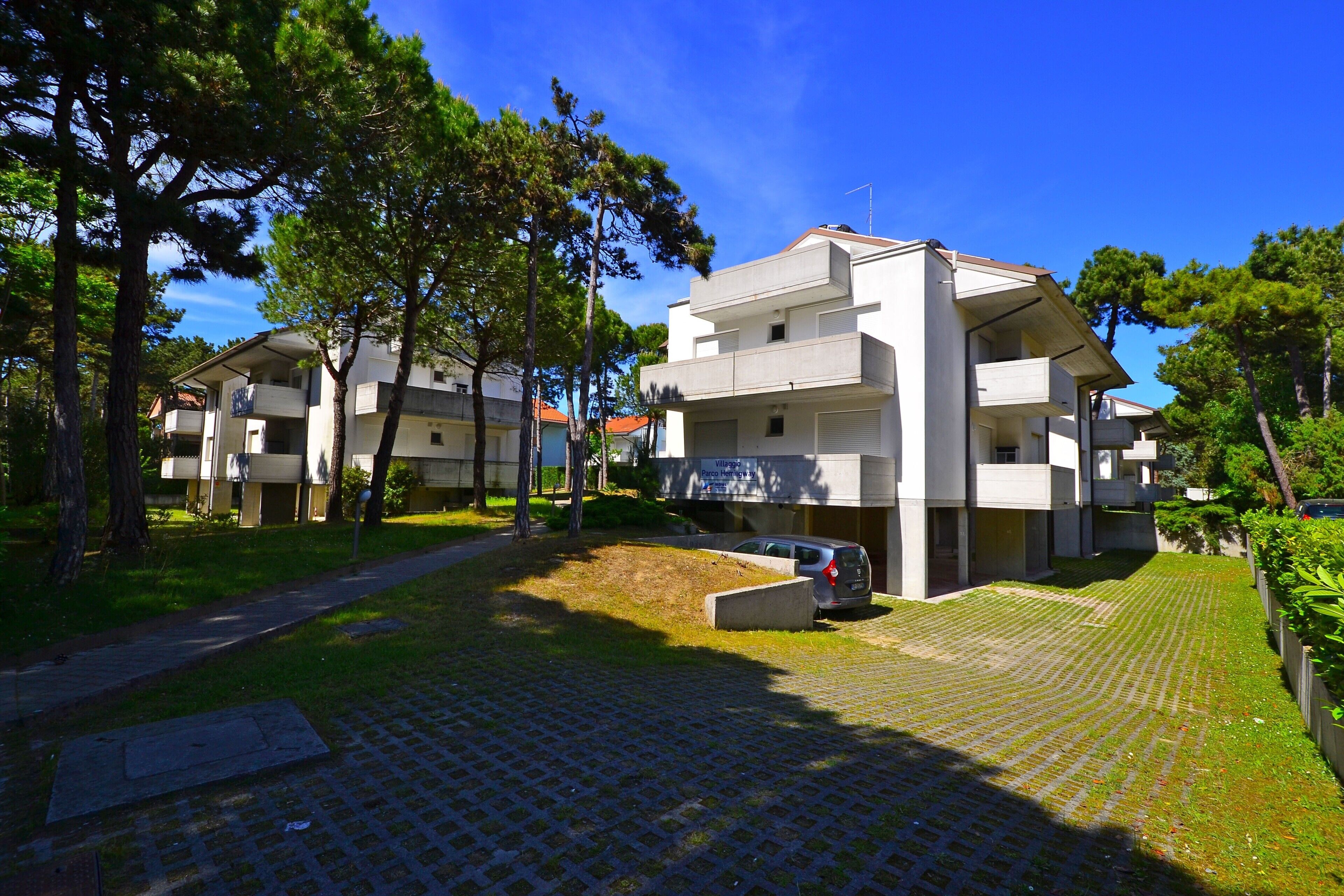 En bostadsbyggnad med en stenlagd innergård, en parkerad bil och träd runt omkring.