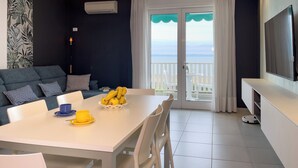 A modern living room with a dining area, a sofa, a TV, and a balcony with a view. - Modern vacation home with a sea view balcony (Lignano Sabbiadoro)