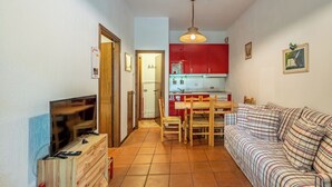 Ein gemütlicher Wohnraum mit Fernseher, Holzmöbeln, einem Esstisch und einer Küchenzeile.