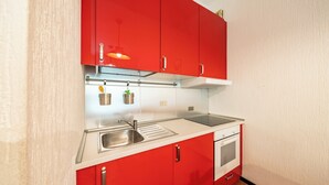 Eine kleine Küche mit roten Schränken, einer Edelstahl-Spüle, einer weißen Arbeitsplatte und einem eingebauten Ofen.