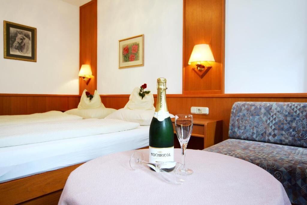 Ein Hotelzimmer mit Bett, Sofa, Tisch, einer Flasche Champagner und einem Glas, sowie Wandleuchten.
