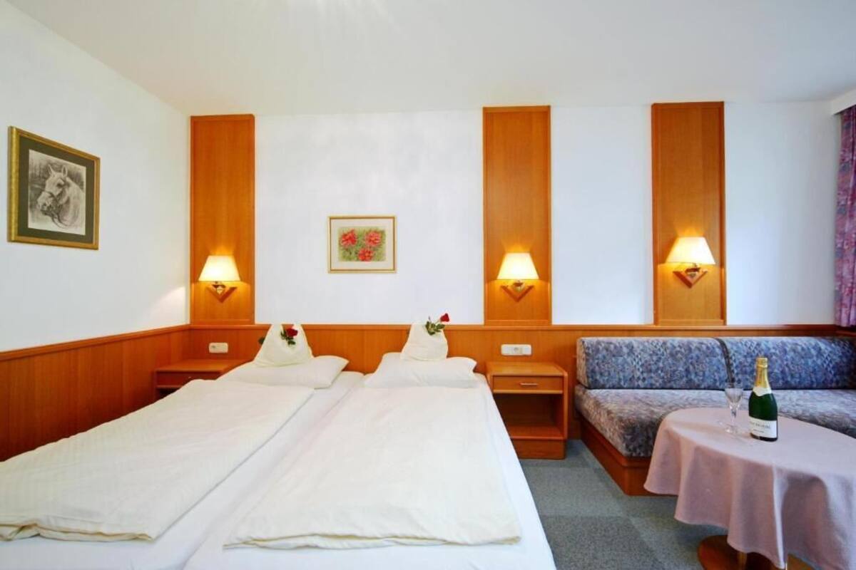A hotel room with two beds, a sofa, a small table with a bottle, and wall-mounted lamps.